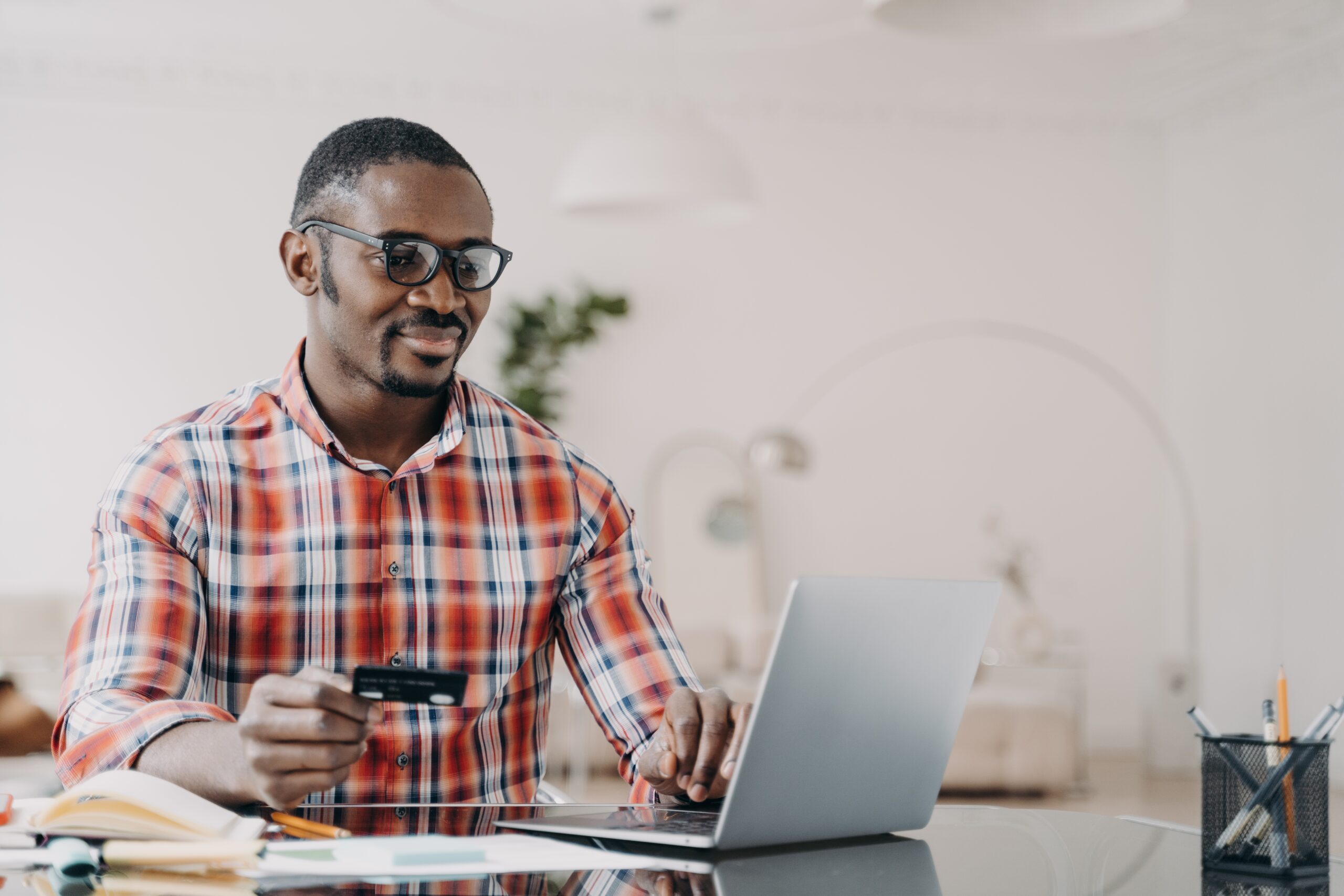 Happy african american man in glasses is purchasing online using laptop and credit card.